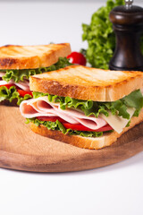 Close-up of two toasted sandwiches with fresh ham, cheese and vegetables on background. Club sandwich and take-away concept. Fast food. 