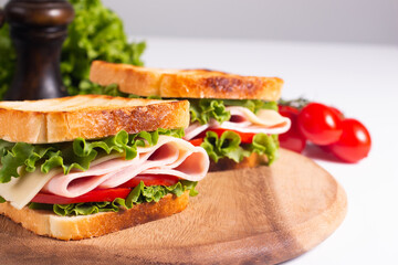 Close-up of two toasted sandwiches with fresh ham, cheese and vegetables on background. Club sandwich and take-away concept. Fast food. 