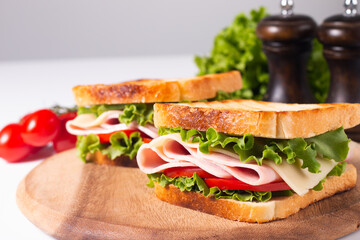 Close-up of two toasted sandwiches with fresh ham, cheese and vegetables on background. Club sandwich and take-away concept. Fast food. 