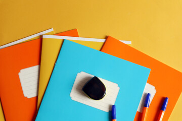 Time to go to school: school notebooks in orange, yellow, blue, sharpener, pens on a yellow...