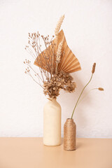 A bouquet of beige flowers and paper palm trees on white wall background