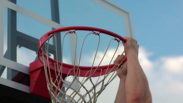 man dunking on a new basketball net and holding onto the ball rim after he makes the dunk