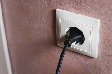 Electric socket on a pink wall. The black wire plug is connected. Renovated backdrop of studio apartment. Blank copy space single white plastic socket