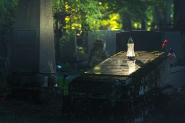 Znicz na cmentarzu postawiony na grobowcu - pada na niego słońce - obrazy, fototapety, plakaty
