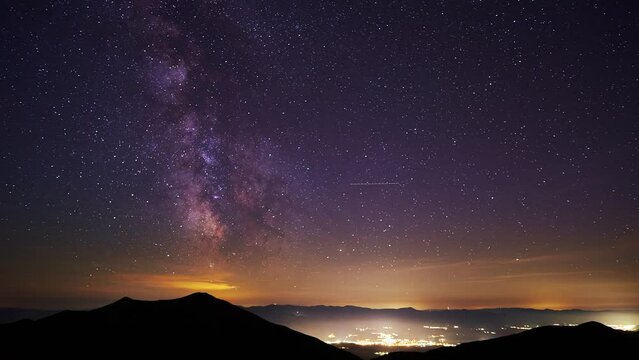 The core of the milkyway in the night sky,the silhouette of the hills and glowing city in the valley