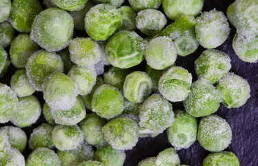 Frozen green garden peas covered in ice on black surface with selective focus