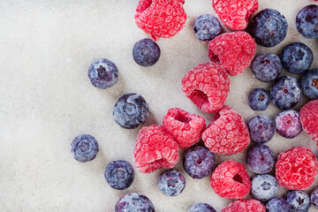 Frozen blueberries and raspberries scattered on light grey with copy space