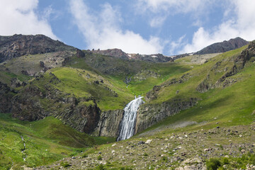The high-altitude waterfall Terskol flowing from the top of a cliff among alpine meadows in a valley in the Elbrus region in the North Caucasus in Russia on a cloudy summer day