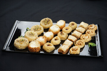 oriental sweets of different types on a large plate on a black background

