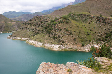 Lake Gizhgit turquoise high in the mountains with hilly shores and a cloudy summer day