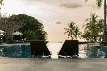 Swimming pool with beach chairs at luxury villa with sunset sky.
