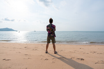 rear view of young asian man in casual shirt standing on the beach on summer vacation