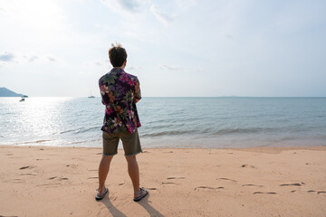 rear view of young asian man in casual shirt standing on the beach on summer vacation