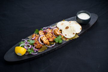 Fototapeta na wymiar fried chicken shish kebab on a wooden board with flatbreads on a black background 