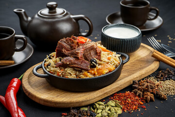 rice pilaf with meat in a round pan on a board with sour cream on a black background macro photo
