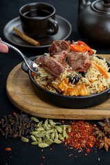 rice pilaf with meat in a round pan on a board with a fork in female hands
