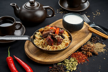 rice pilaf with meat in a pan on a black board on a black background with a teapot
