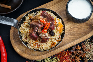 rice pilaf with meat in a pan on a black board on a black background with a teapot macro photo
