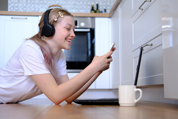 A young girl of 15-18 years old lies on the floor with a laptop and a telephone