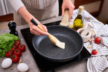Woman smear olive oil on frying pan with silicone brush at domestic kitchen