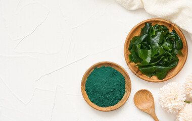 top view or flat lay laminaria or kelp seaweed and spirulina powder in wood plate and spoon background. spirulina powder with konbu and alga food on white table background.                         - obrazy, fototapety, plakaty