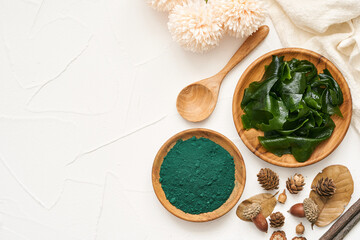 top view or flat lay laminaria or kelp seaweed and spirulina powder in wood plate and spoon background. spirulina powder with konbu and alga food on white table background.                         - obrazy, fototapety, plakaty