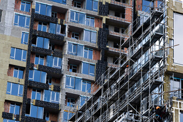 Obraz premium Construction of scaffolding and installation of glass facade panels against the backdrop of a new building