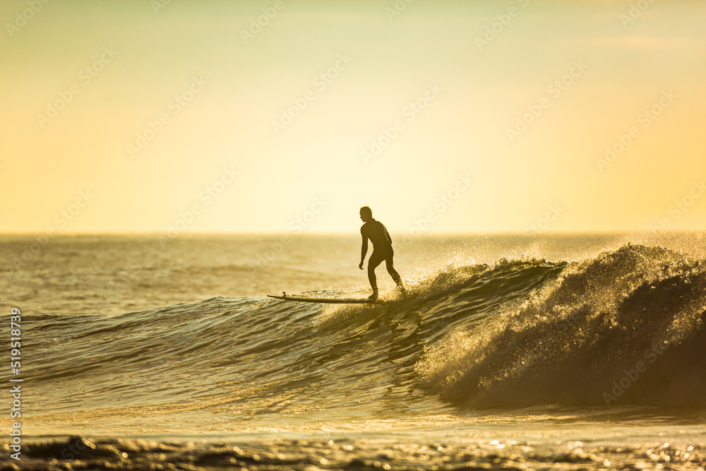 Wall mural An unidentified surfer rides a big wave with foam at sunset. Silhouette of a man surfing. Extreme water sport concept