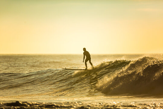 An unidentified surfer rides a big wave with foam at sunset. Silhouette of a man surfing. Extreme water sport concept