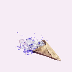 Golden Ice cream cone on pastel purple background with purple glitter and ice cubes. Minimal summer food concept