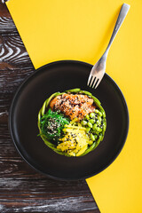 Appetizing bowl with salmon and vegetables sprinkled with sesame seeds on a yellow background