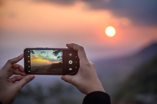 woman hands holding mobile phone to taking sunset photo
