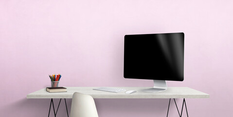 Blank computer display on work desk with pens and book beside. Pink wall in background