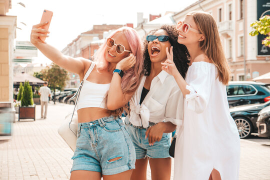 Three young beautiful smiling hipster female in trendy summer clothes.Sexy carefree multiracial women posing on the street background.Positive models having fun. Taking selfie photos