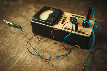 An old electric voltage tester in vintage style. Antique measuring device with wires on a wooden...