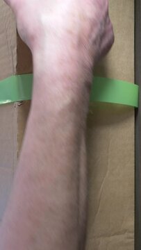 Vertical video social media format &ndash; Closeup of hands using scissors to cut a piece of holding tape around a large cardboard shipping box, then prising open a glued retaining flap on the side.