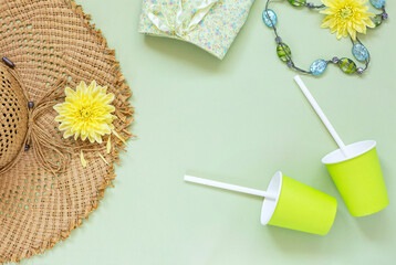 Summer background. Straw hat, skirt, beads, yellow flowers and  paper cups on green background. The concept of summer holidays, travel, life style. Flat lay, top view..