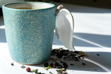 A cup of herbal tea with various herbs on white background with shadows