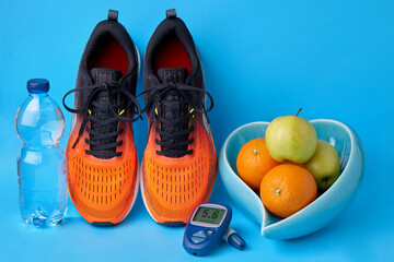 Orange sneakers, glucometer, bottle of drinking water and fruits on blue background