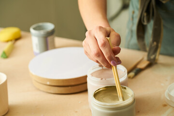 Close-up of girl painting clay mug with glaze. Woman coloring pottery in workshop with a paintbrush. Painter in green apron glazing clay pot.