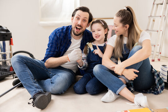 Young family dressed in denim style is sitting on floor. Wife husband and child recently bought new, big, dream house. Everyone is very happy about this. In background are things to repair.