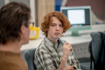 Ginger boy sitting next to teacher and looking interested