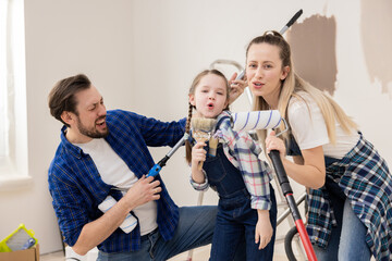Man beautiful blonde and their daughter are singing and rejoicing that they have finally chosen desired color to repaint living room. In the background behind the people there is ladder.