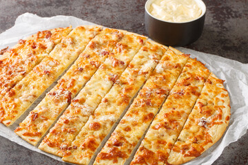 Pizza Garlic Fingers with mozzarella cheese, bacon and herbal butter and Donair Sauce close-up on paper on the table. horizontal