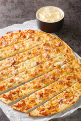 Delicious garlic fingers with herb butter and melted mozzarella cheese closeup in the paper on the table. Vertical