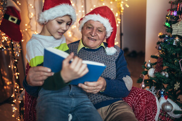 Fototapeta na wymiar Grandfather and grandson sitting on chair and reading book during christmas.