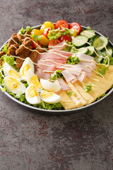 Chef salad is an American salad consisting of boiled eggs, more varieties of meat, tomatoes, cucumbers, and cheese, all placed upon a bed of tossed lettuce closeup in the plate on the table. Vertical