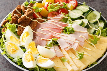 Classic chef salad is a greens salad that is served with assorted meats, cheese, and vegetables and coasted in a homemade dressing closeup in the plate on the table. Horizontal