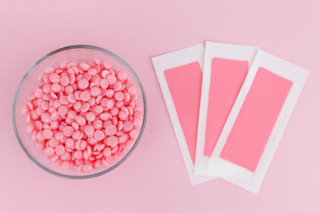 Beautiful pink wax granules and wax depilatory strips for delicate areas on a pink background. Epilation, depilation, unwanted hair removal. Top view. - obrazy, fototapety, plakaty