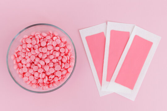 Beautiful pink wax granules and wax depilatory strips for delicate areas on a pink background. Epilation, depilation, unwanted hair removal. Top view.